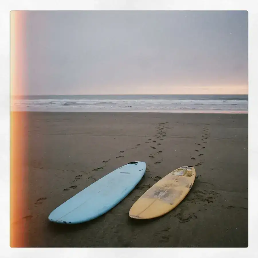 Twee surfplanken naast elkaar op een verlaten strand, twee sporen voetstappen naar zee