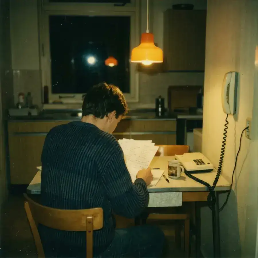Een jonge man werkt s nachts aan de keukentafel, papieren onder een oranje lamp